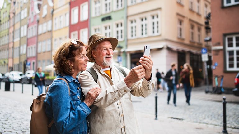 An old couple traveling Europe searching for how much do I need by their smartphone