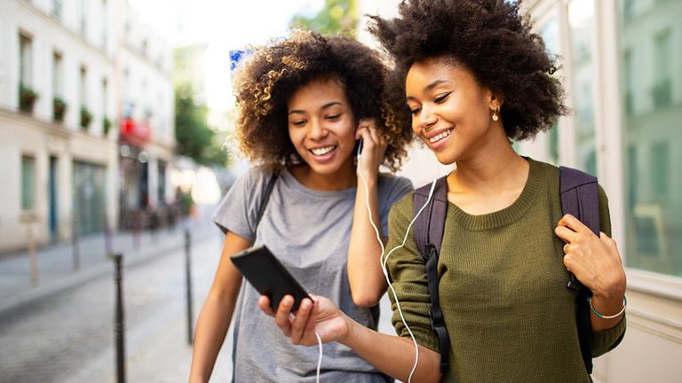 Two female friends walking down the street while listening to music together